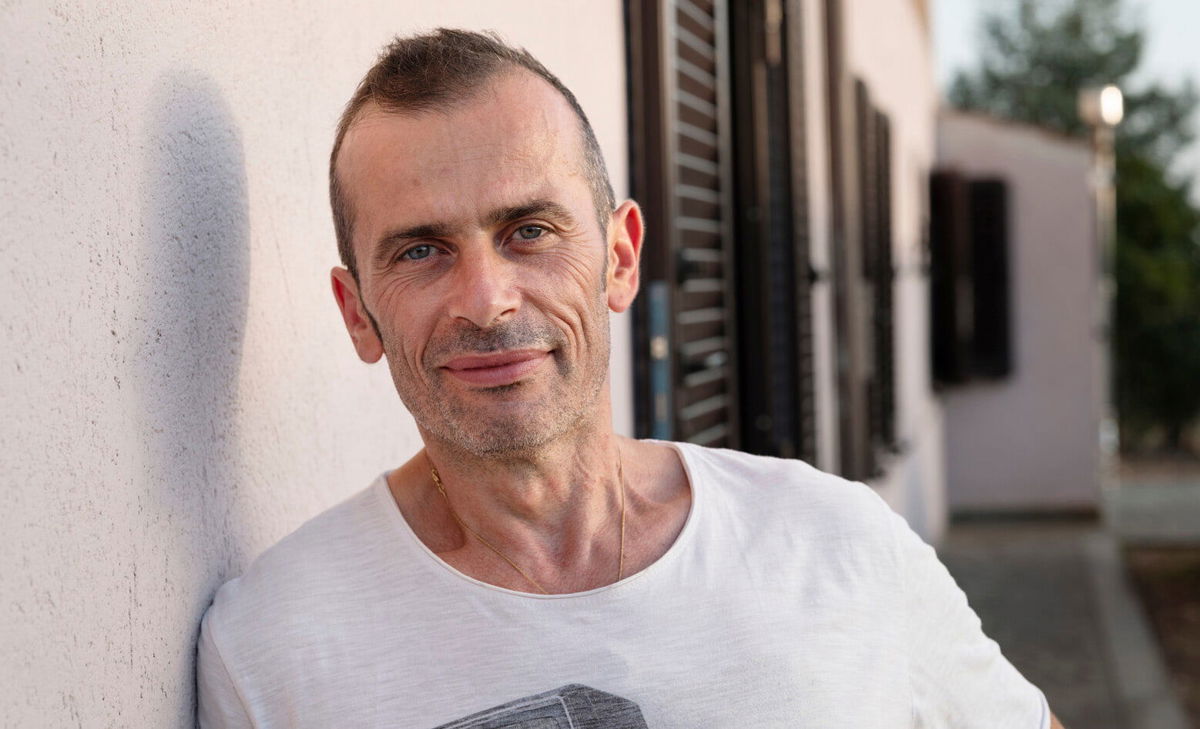 Foto di Andrea davanti alla sua casa. Andrea convive con la SM e avrebbe voluto sapere qualcosa in più su cosa aspettarsi riguardo ai problemi alla vescica e all'intestino.  