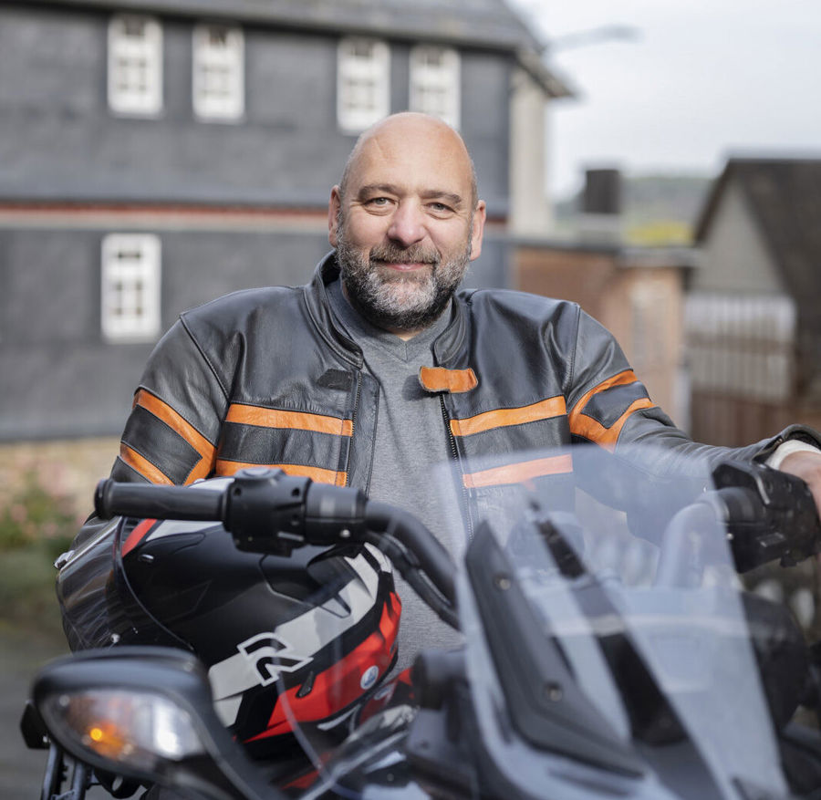 Foto ritratto di Michael seduto sulla sua moto. Michael convive con la sclerosi multipla e soffre di problemi alla vescica. Ha scoperto di avere una vescica iperattiva e di dover urinare più spesso. 
